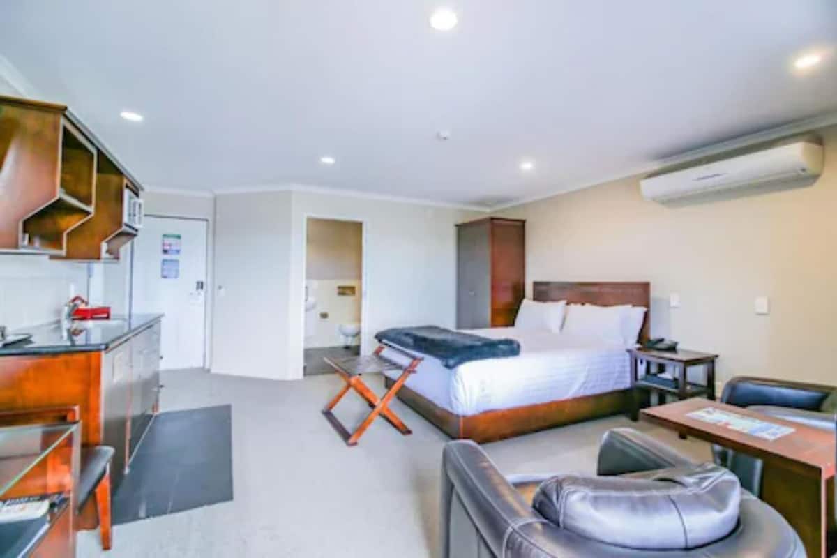Una habitación de hotel con cama, escritorio, silla, sofá y kitchenette.