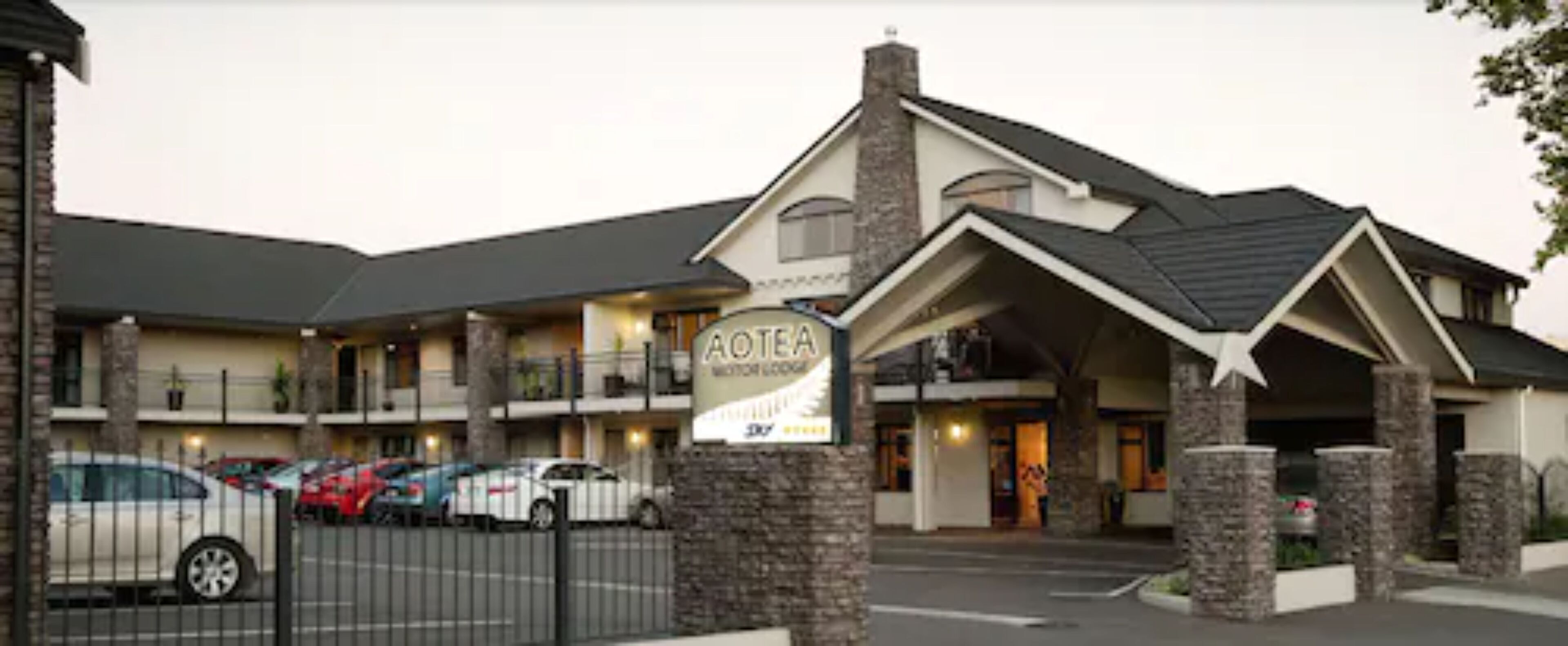 A motel with a signboard, multiple parking spaces, and a brick facade.