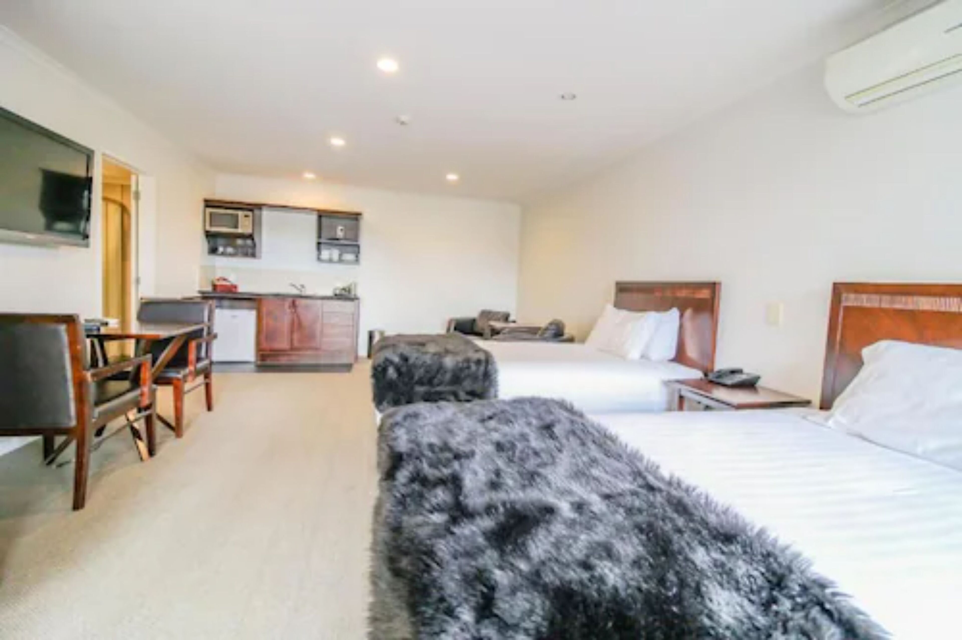 Una habitación de hotel con cama, escritorio, silla, kitchenette pequeño y televisión.