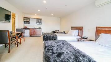 Una habitación de hotel con cama, escritorio, silla, kitchenette pequeño y televisión.