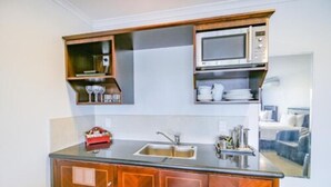 A compact kitchen with a built-in microwave, a double sink, and wooden cabinets. - Aotea Motor Lodge (Whanganui)