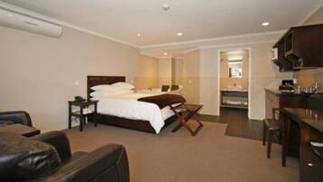 A hotel room with a bed, a desk, a chair, a sofa, and a bathroom visible through an open door.