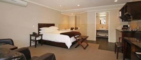 Habitación de hotel con cama, escritorio, sillón, sofá y baño visible a través de una puerta abierta.