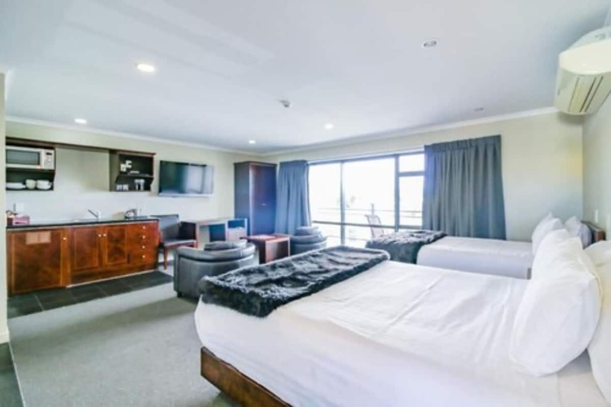 Habitación de hotel con una cama grande, un escritorio con silla, televisión y ventana con cortinas.