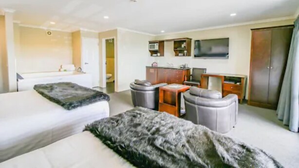 A hotel room with two beds, a kitchenette, a TV, and a wardrobe. - Aotea Motor Lodge (Whanganui)