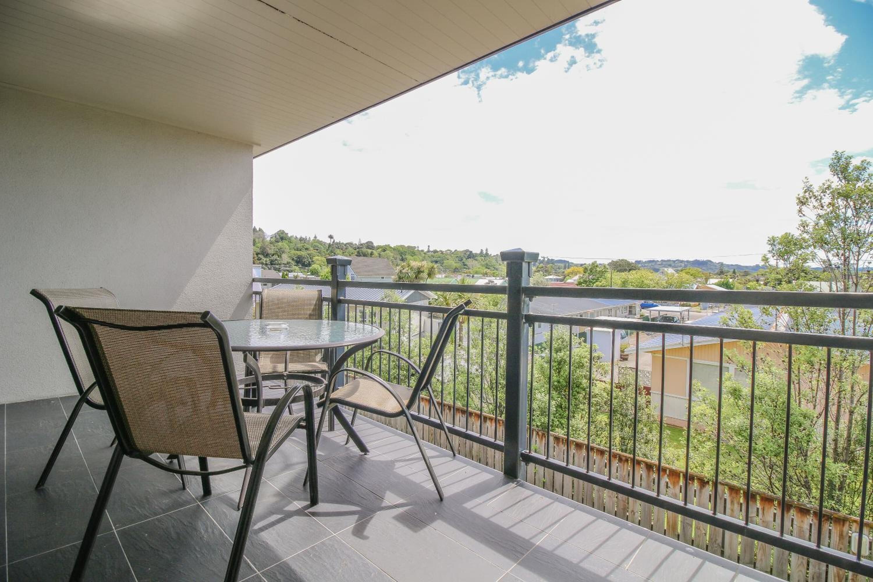 A balcony with a table and chairs, a view of a cityscape, and a railing.