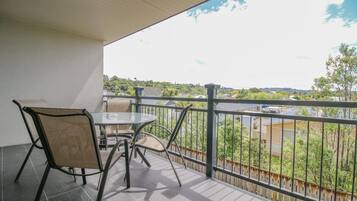 A balcony with a table and chairs, a view of a cityscape, and a railing.