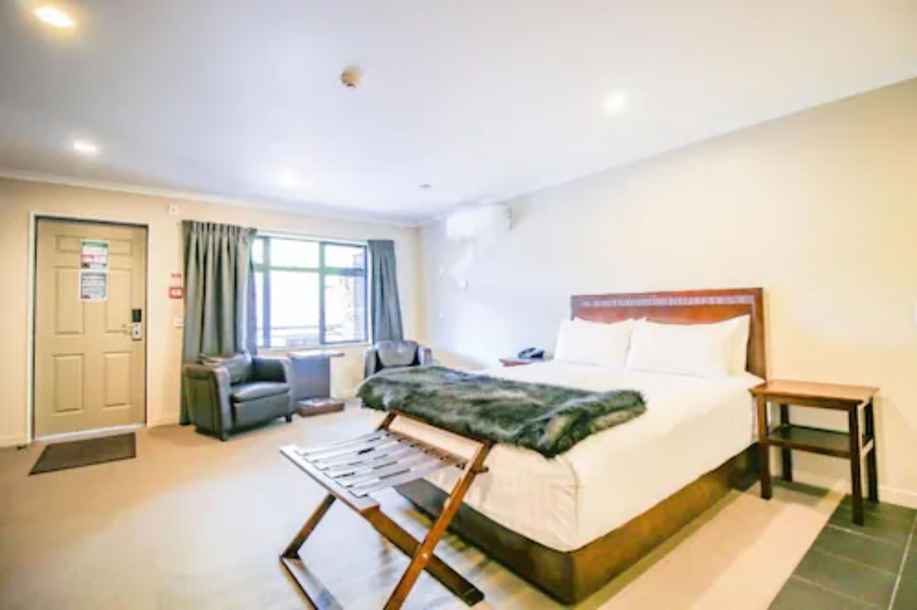 A hotel room with a bed, a desk, a chair, a window with curtains, and a door.