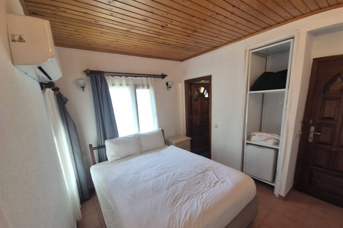 A bedroom with a bed, a wardrobe, a door, and a window with curtains.