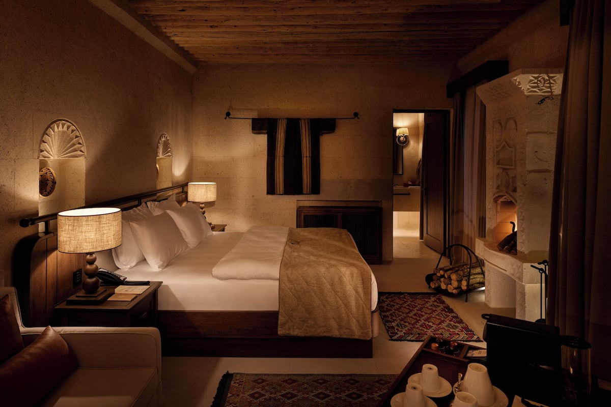 Ett hotellrum med ett träpanelat tak, en säng med vita sängkläder, ett sängbord med en lampa, en spegel och utsikt in i badrummet.