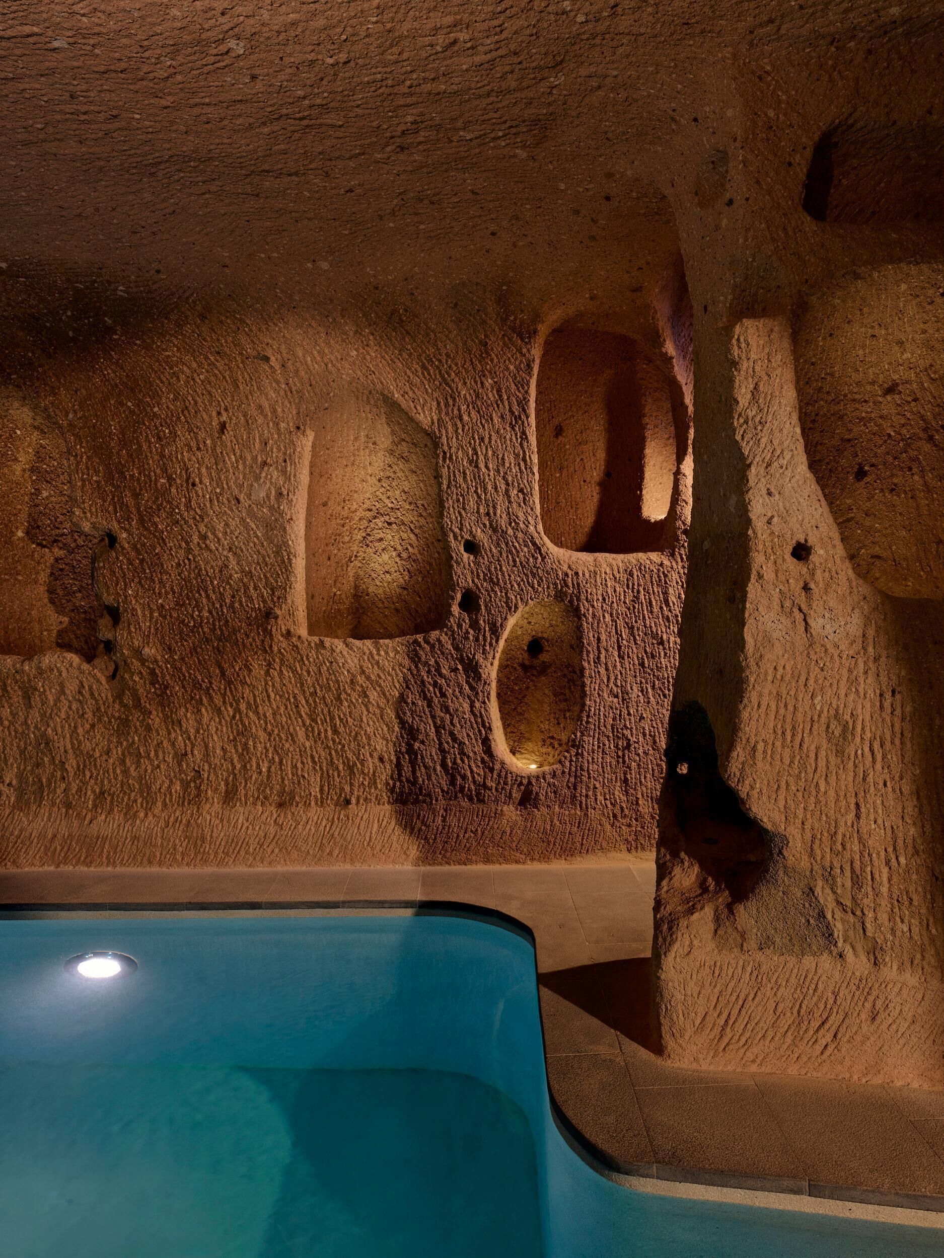 A room with a pool, a stone wall, and a ceiling with a circular skylight.