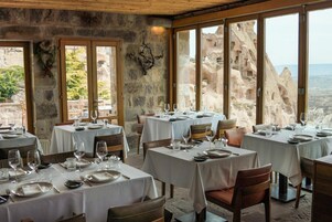 A restaurant with tables set for dining, stone walls, and large windows offering a view of rocky terrain.