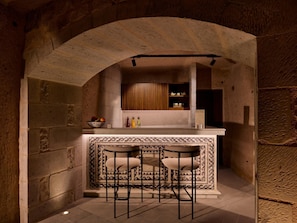 An arched stone kitchen with a bar area, stools, and a tiled backsplash.