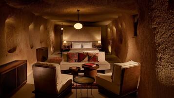 A cozy, dimly lit room with a large bed, two armchairs, a small table, and a hanging light fixture.