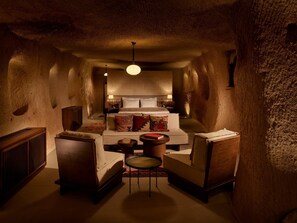 A cozy, dimly lit room with a large bed, two armchairs, a small table, and a hanging light fixture.