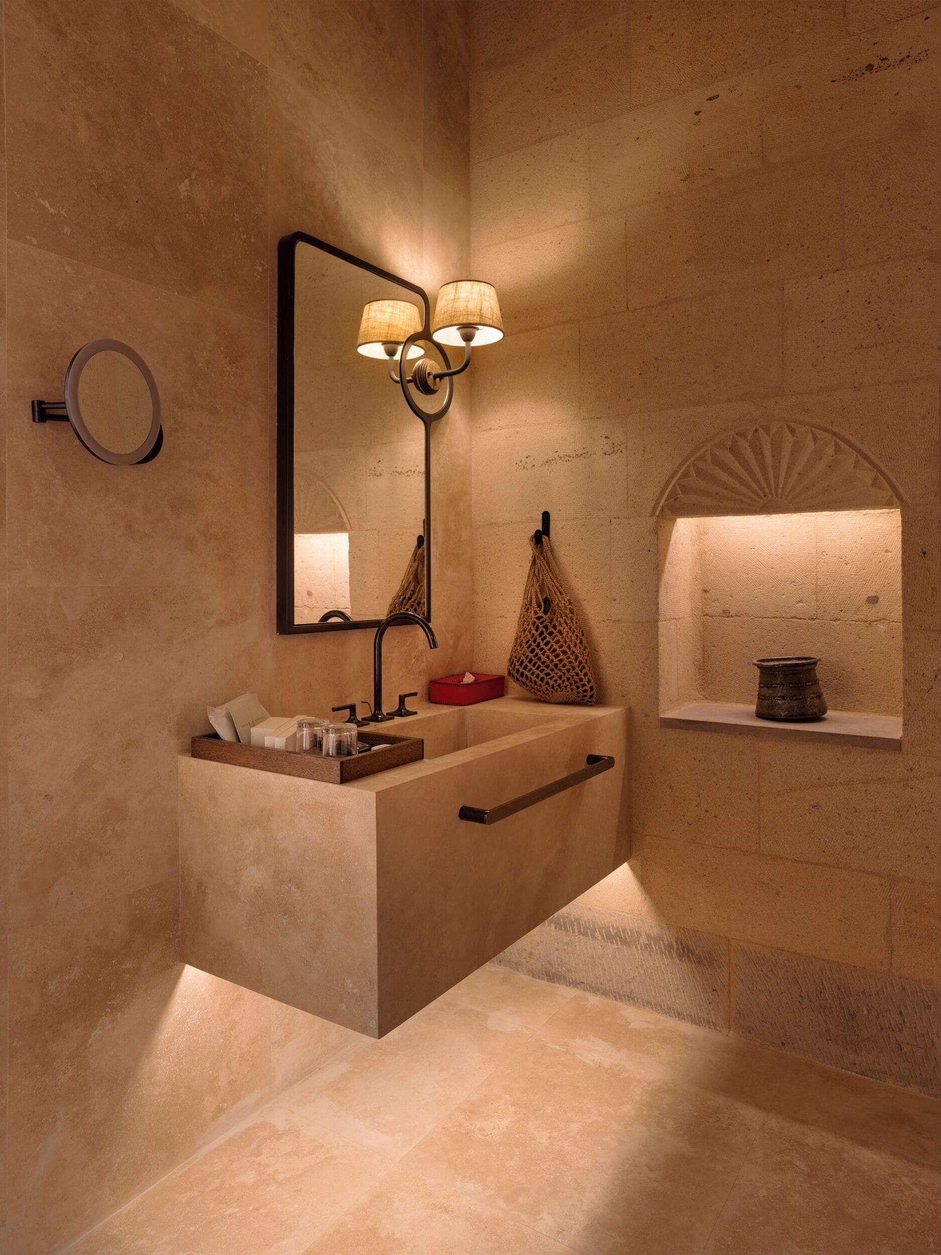 A modern bathroom with a large sink, a mirror, and a wall-mounted lamp.