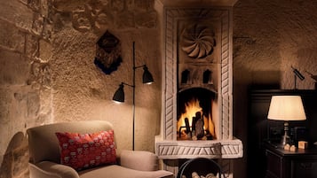 Una habitación acogedora con chimenea de piedra, un sofá con un cojín rojo y una alfombra estampada.