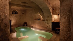 Ein Zimmer mit Steinsäulen, einem zentralen Pool, gewölbten Decken und einem kleinen Tisch.
