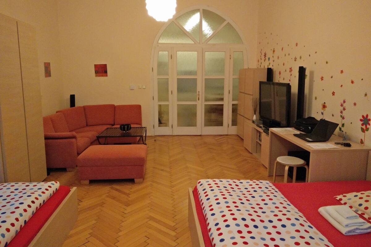 Une chambre d'hôtel avec un canapé, un bureau avec un ordinateur, une télévision et deux lits avec une literie à motifs à pois.