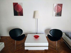 A modern room with a white square table, two black chairs, a red bowl, and two abstract paintings on the wall. - Apartments Tynska 7 (Prague)