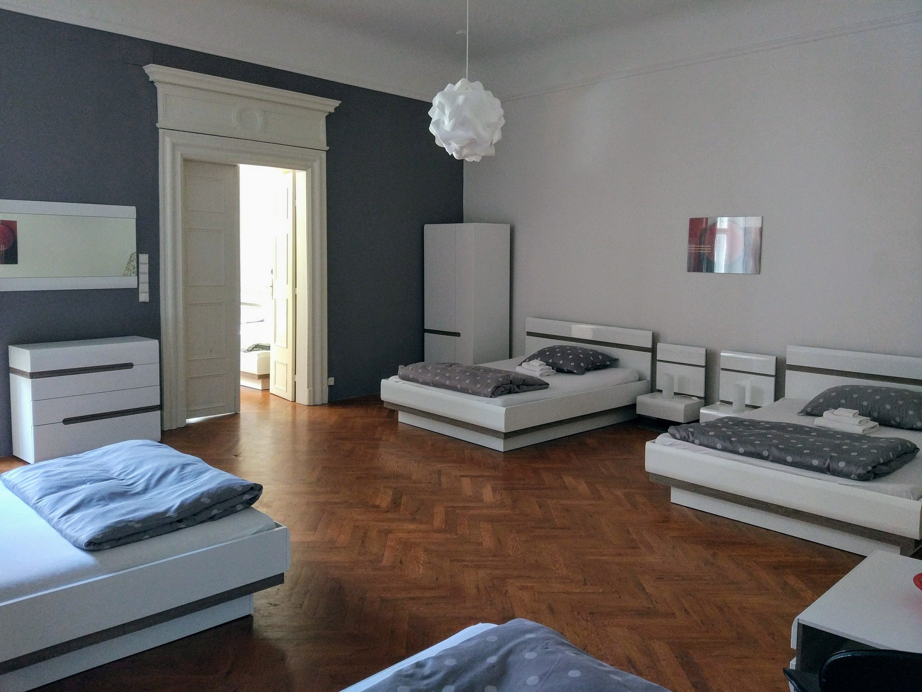 A modern bedroom with a large bed, a smaller bed, a wardrobe, and a desk.
