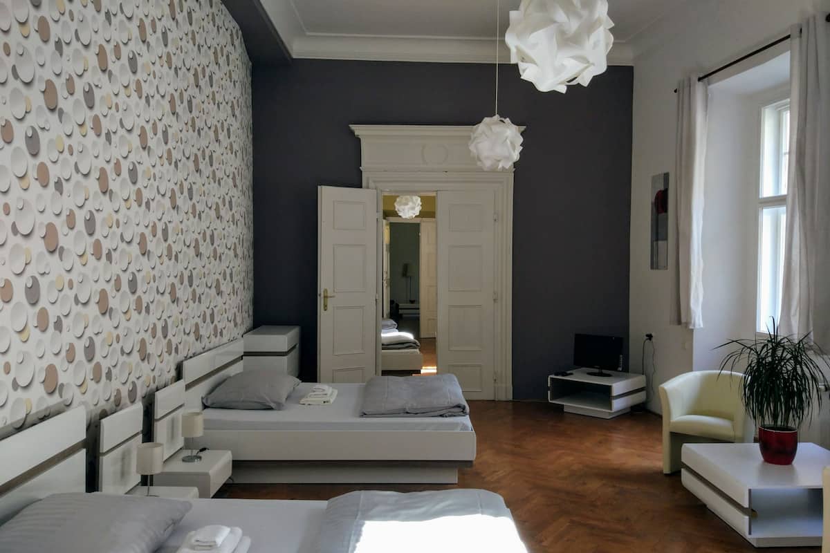 Une chambre moderne avec un grand lit, un plus petit lit, une télévision, une chaise et une plante.
