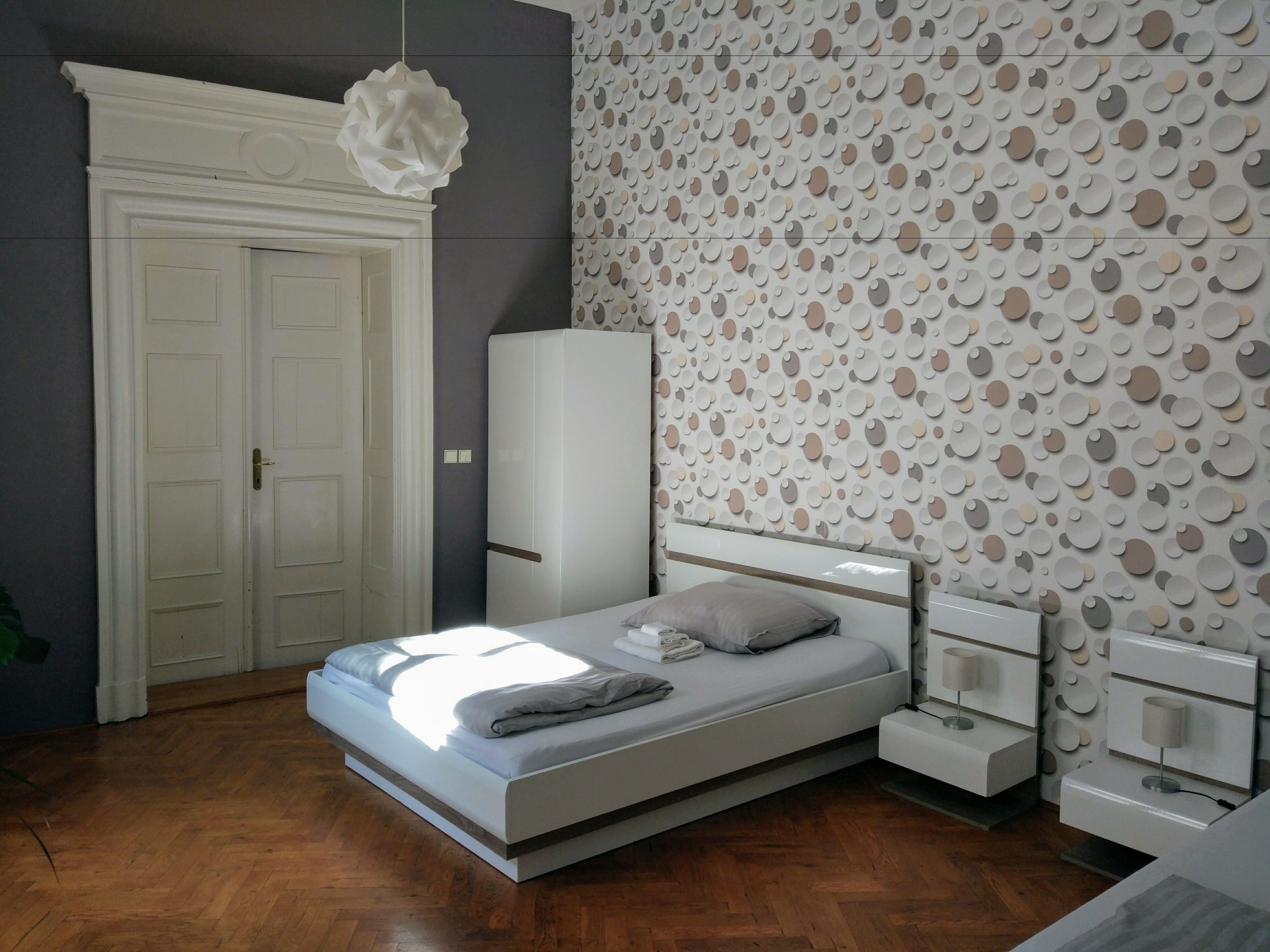 A bedroom with a bed, bedside tables, a wardrobe, and a wall with circular patterns.