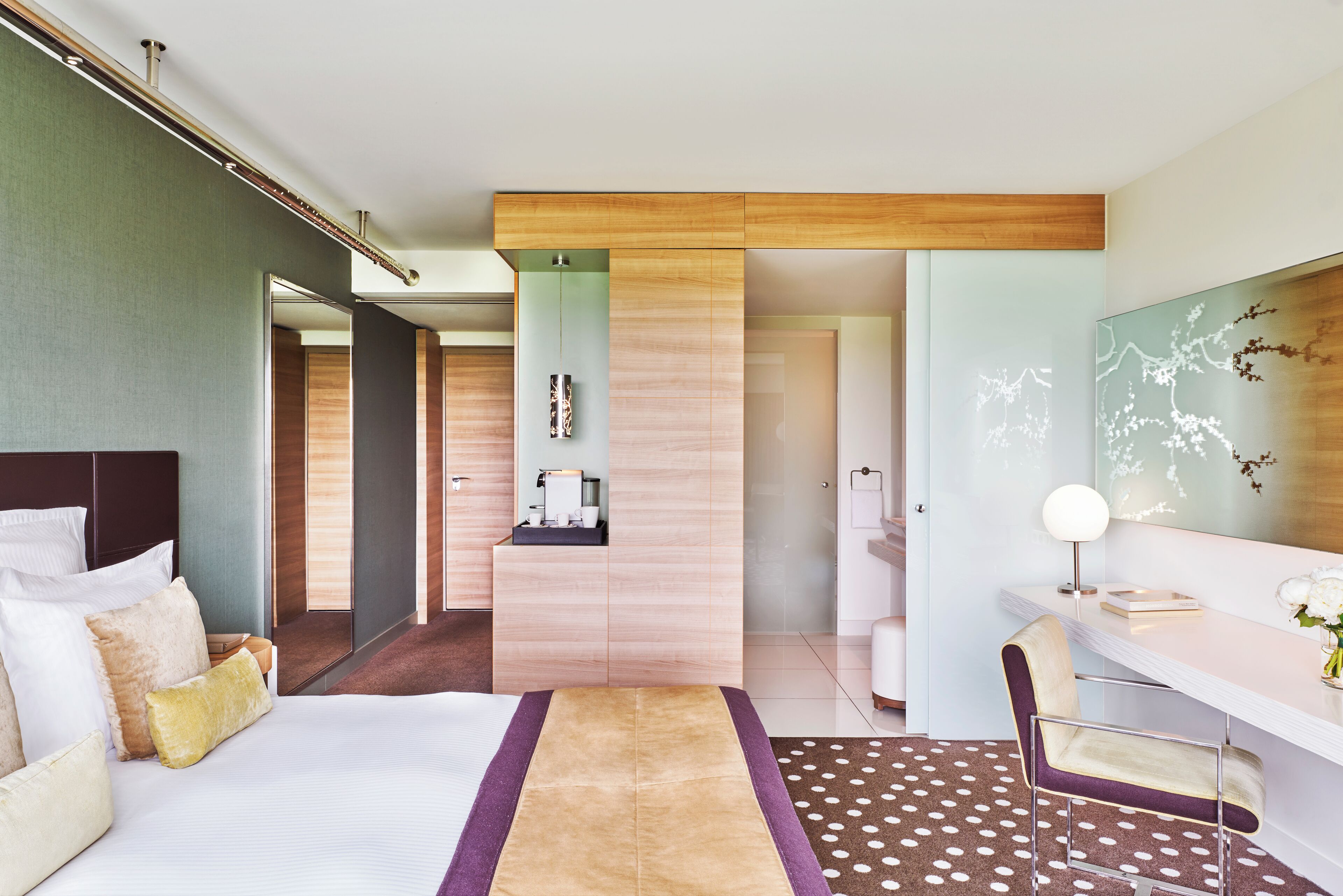 Quarto de hotel moderno com uma cama grande, uma escrivaninha e um banheiro visível por uma porta aberta.