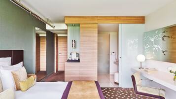 Quarto de hotel moderno com uma cama grande, uma escrivaninha e um banheiro visível por uma porta aberta.