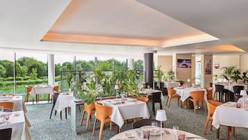 A restaurant with round tables, chairs, and potted plants.