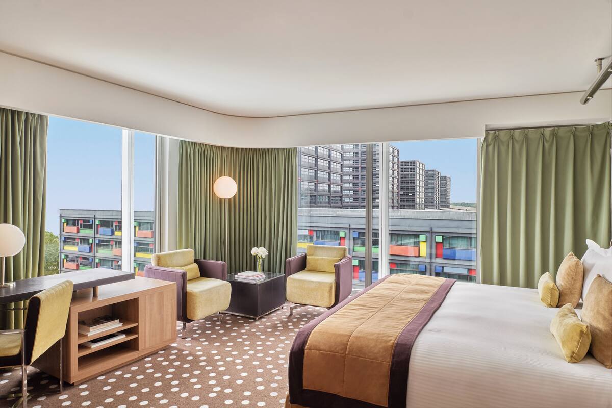 A hotel room with a bed, a desk, two chairs, a coffee table, and a view of a high-rise building.