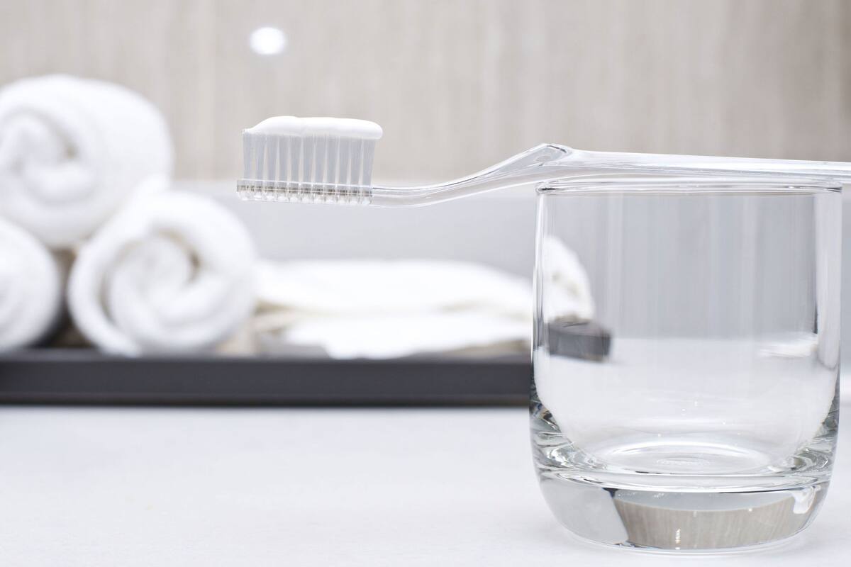 A clear glass of water with a toothbrush inserted into it, and rolled white towels in the background.