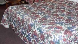 A hotel room with a large bed, a chair, a table, and two wall lamps. - Royal Inn Knoxville Airport Alcoa (Alcoa)