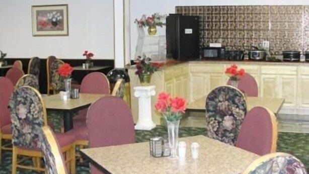 A restaurant with multiple tables and chairs, a ceiling fan, and a kitchen area in the background. - Royal Inn Knoxville Airport Alcoa (Alcoa)