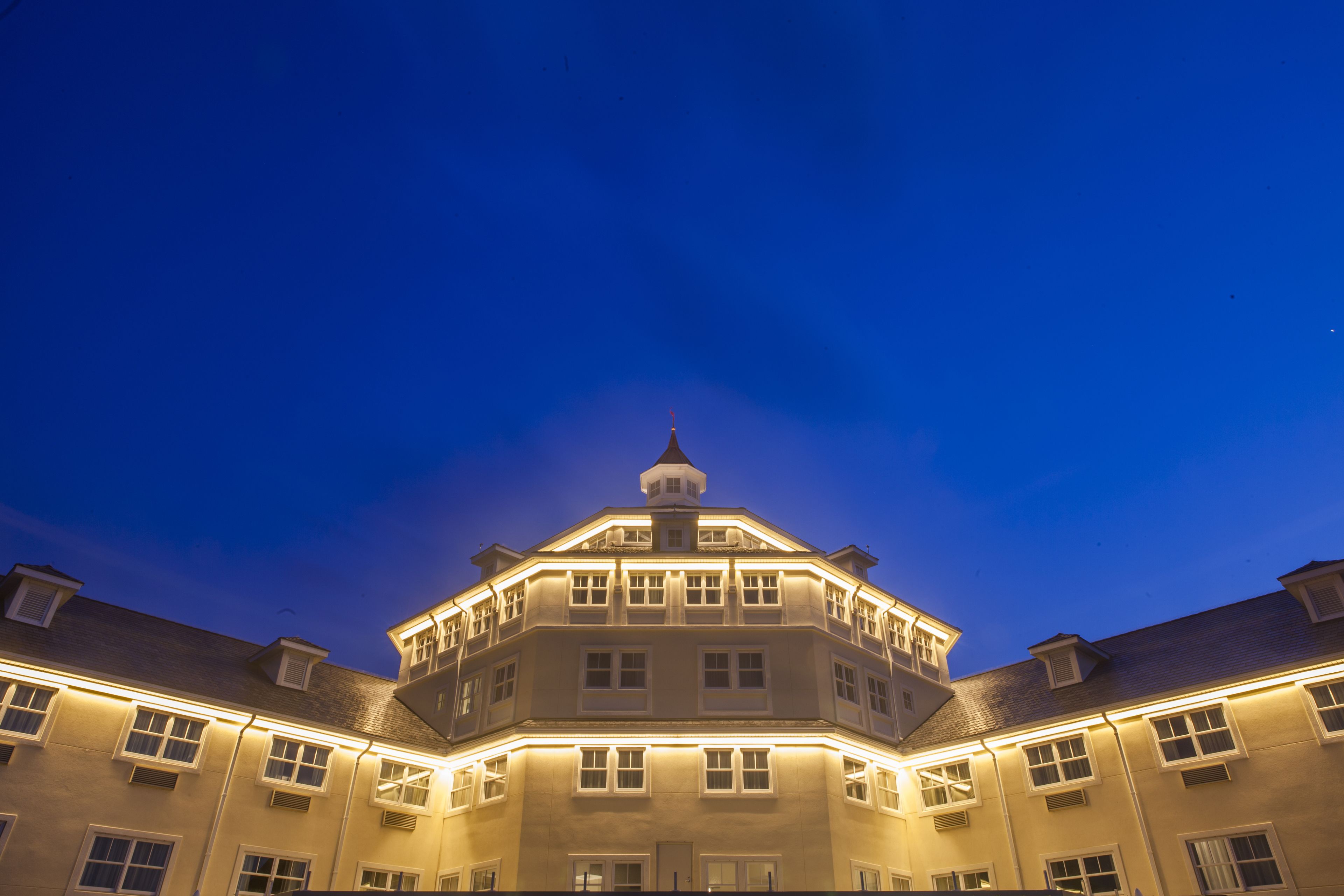 A multi-story building with a corner turret and illuminated windows at night.