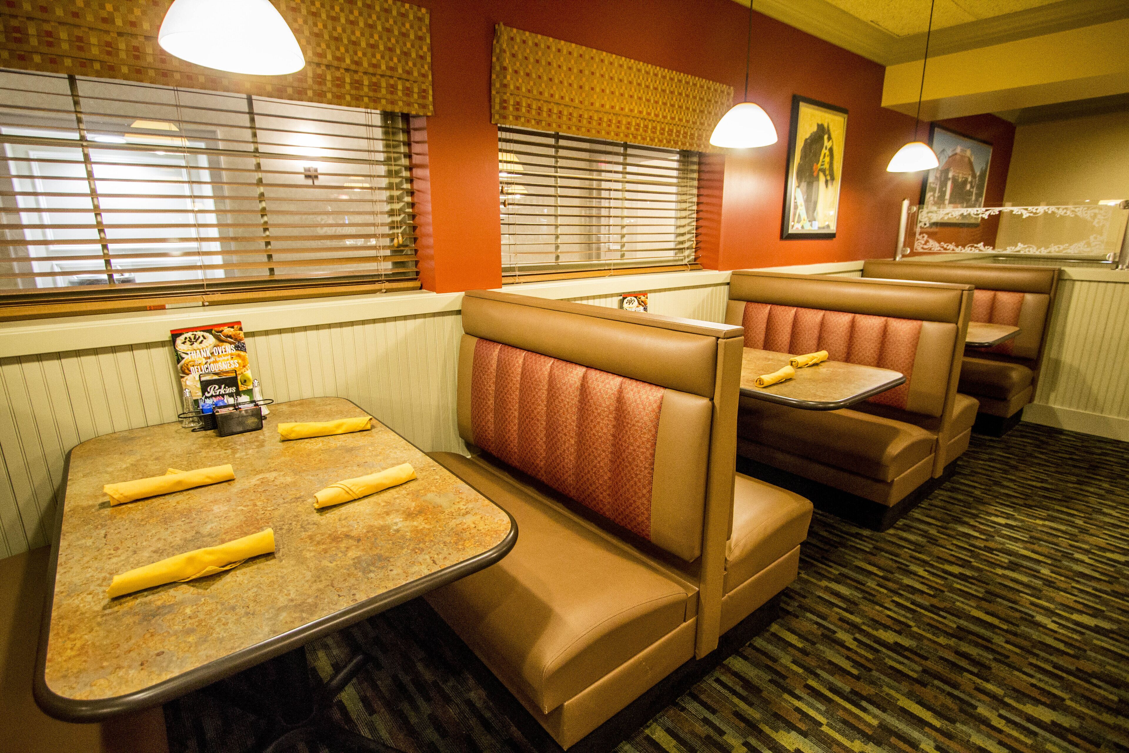 A restaurant with booths and a table, featuring a menu and napkins on the table.