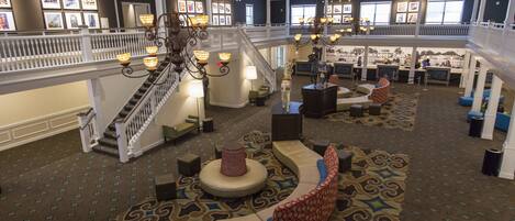 A spacious lobby with a central seating area, a staircase, and a second-floor balcony.