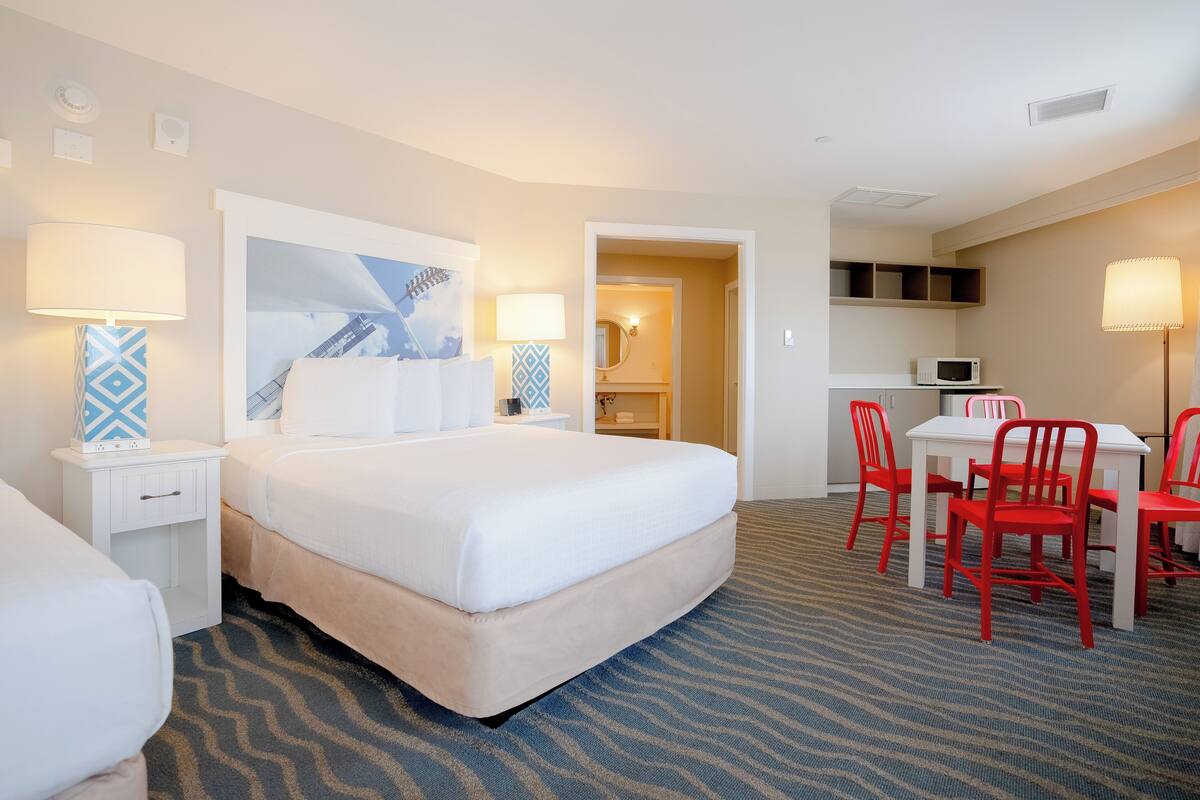Habitación de hotel con una cama grande, un escritorio con sillas rojas, un microondas y un baño visible a través de una puerta abierta.