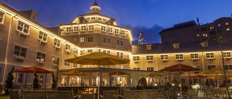 A hotel with outdoor seating and umbrellas, a prominent tower, and a Ferris wheel in the background.