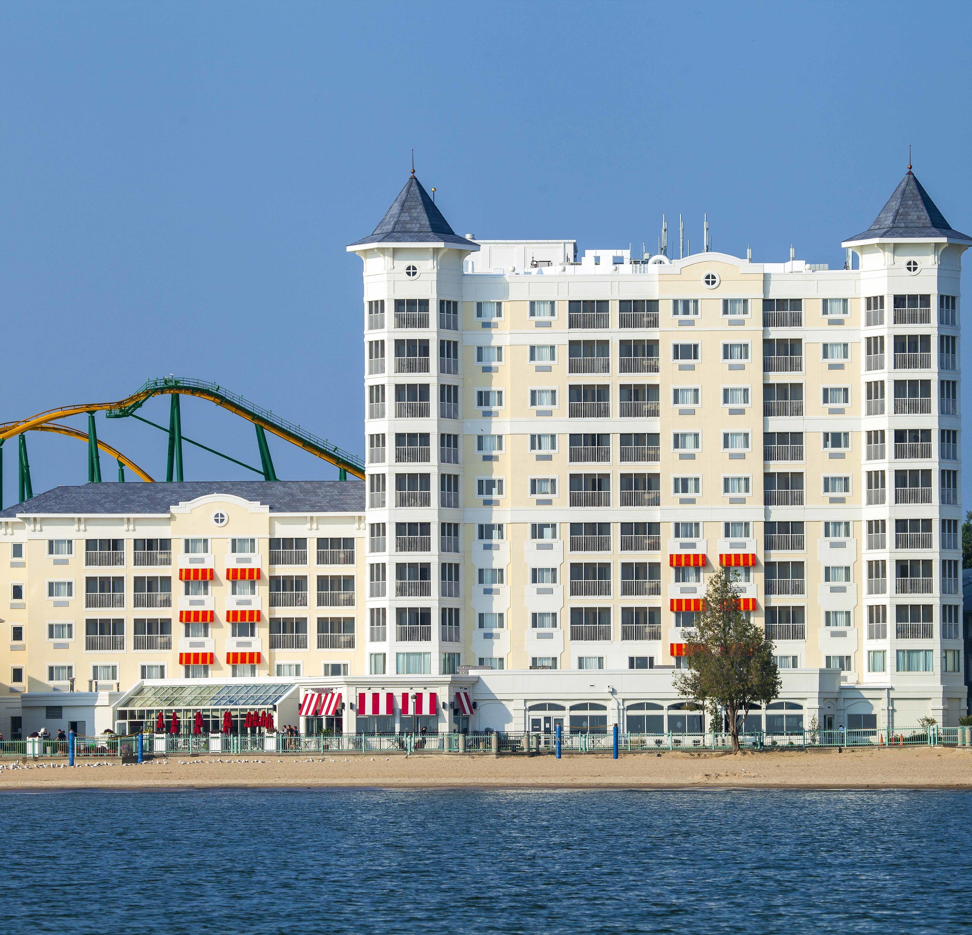 Ein mehrstöckiges Hotel mit Balkonen, einer Strandlage und einer Achterbahn im Hintergrund.