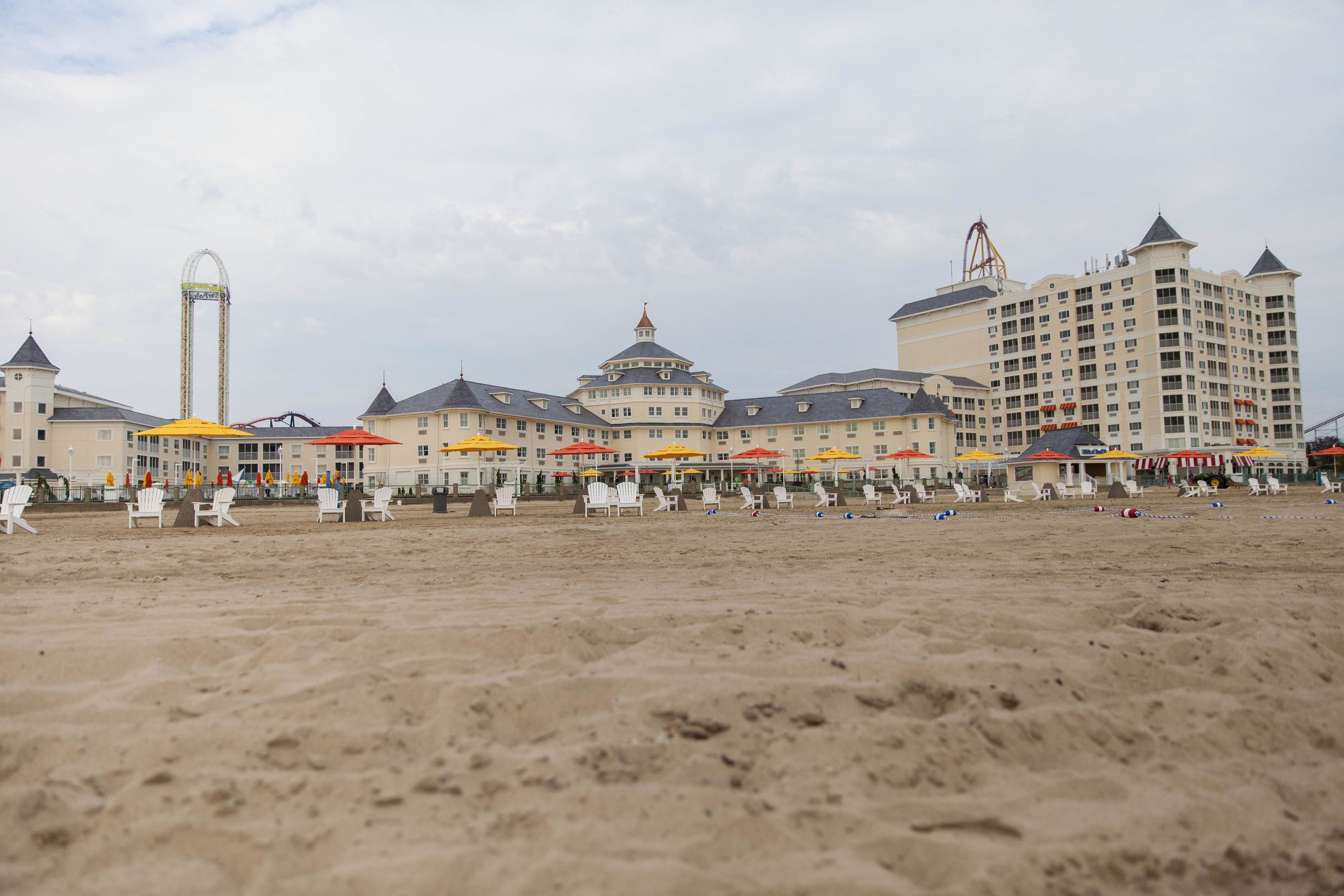 Een strandhotel met meerdere verdiepingen, buiten zitgedeeltes met parasols, en een opvallende attractie in het pretpark op de achtergrond.