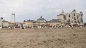 Een strandhotel met meerdere verdiepingen, buiten zitgedeeltes met parasols, en een opvallende attractie in het pretpark op de achtergrond.