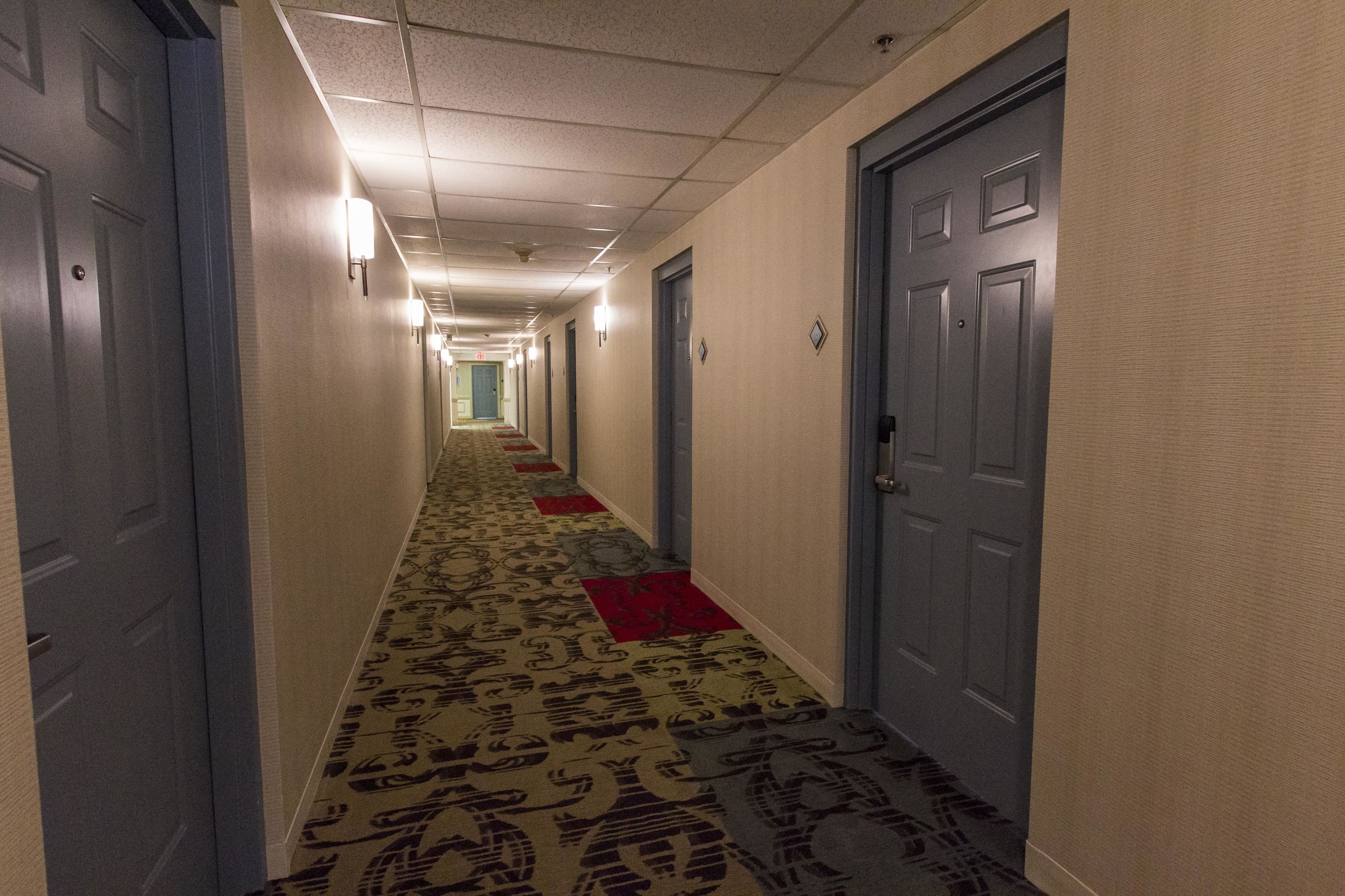A hotel hallway with carpeted floors, doors on both sides, and a red carpet runner down the center.
