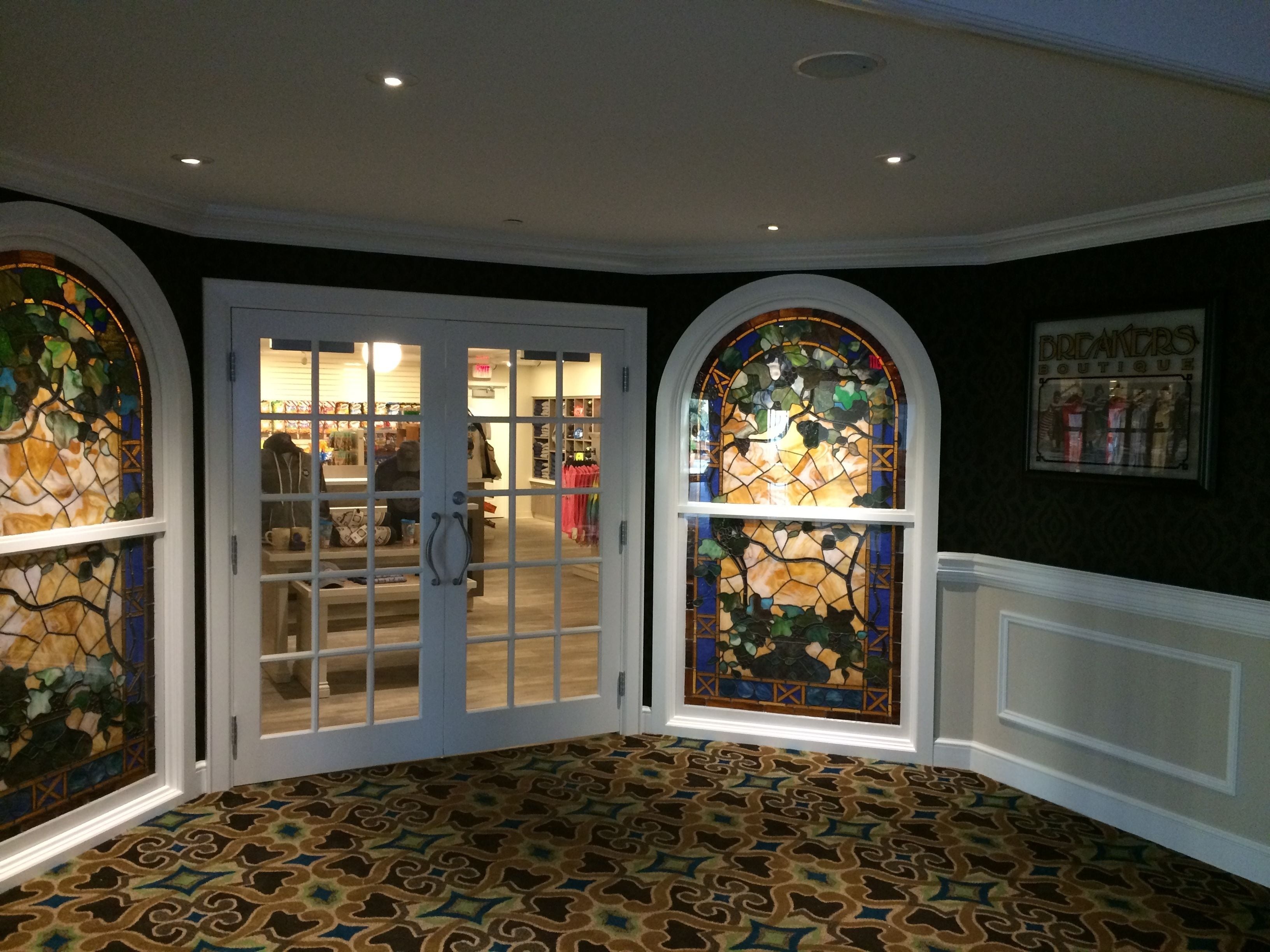 A room with a patterned carpet, a glass door leading to a store, and a stained glass window.