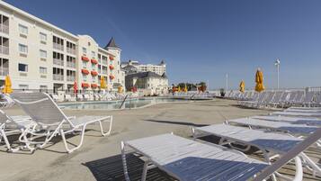 Un hotel con piscina, sillones de descanso blancos y sombrillas amarillas.