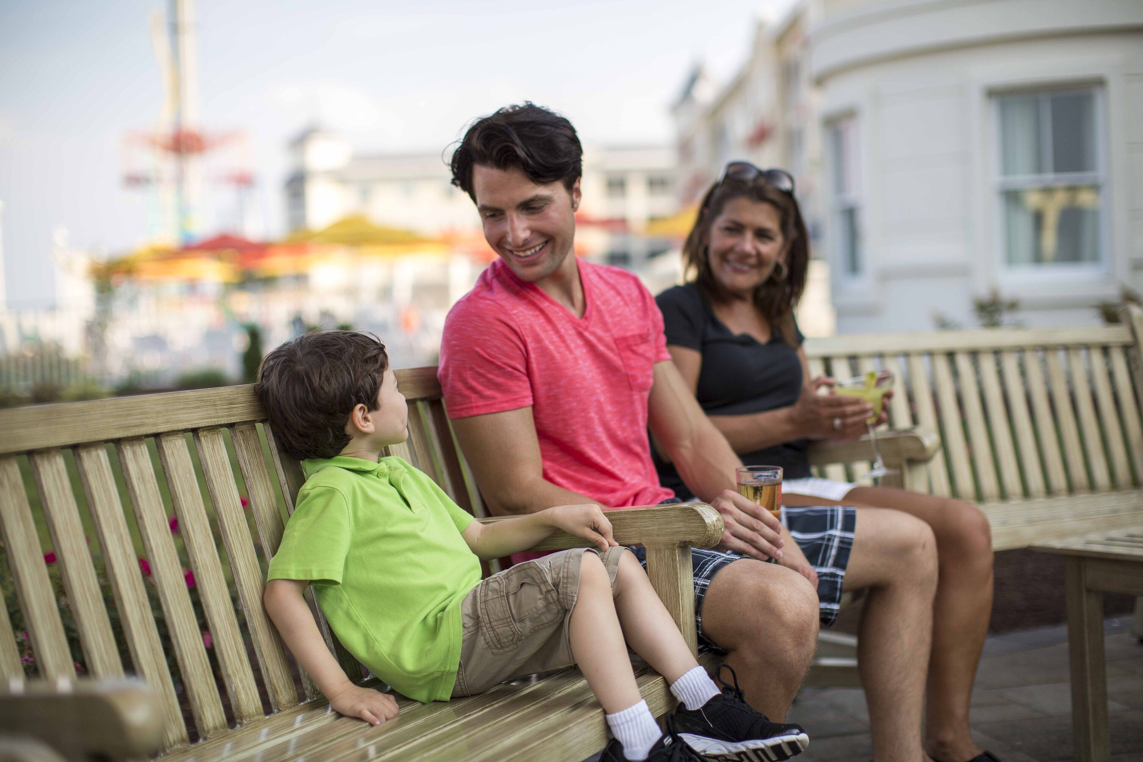 Une famille est assise sur un banc en bois, à l'extérieur.