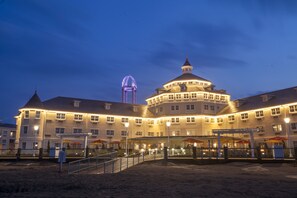 A large, multi-story hotel with a distinctive circular tower, a covered outdoor area with umbrellas, and a Ferris wheel in the background. - Cedar Point's Hotel Breakers (Sandusky)