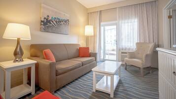 A hotel room with a beige sofa, two side tables with lamps, a white armchair, a small white table, and a patterned carpet.
