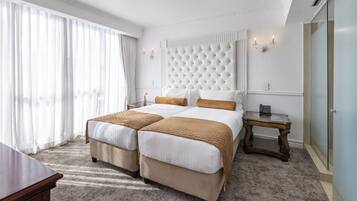A hotel room with a large bed, two bedside tables, a small table, and a large window with curtains.