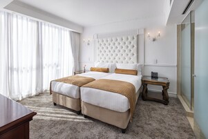 A hotel room with a large bed, two bedside tables, a small table, and a large window with curtains.